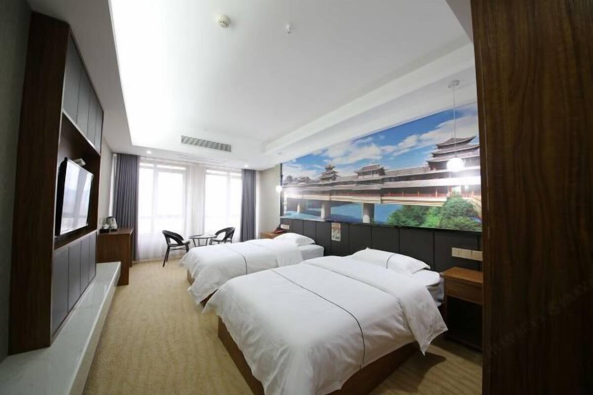 Habitación de hotel con dos camas, televisión, escritorio y un gran mural de un edificio tradicional.