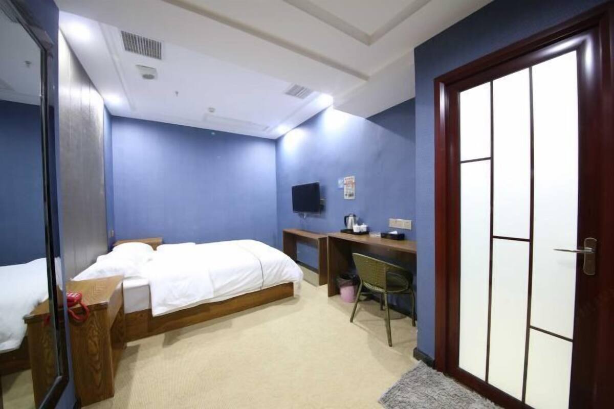 Una habitación de hotel con cama, escritorio, silla, televisor y armario.