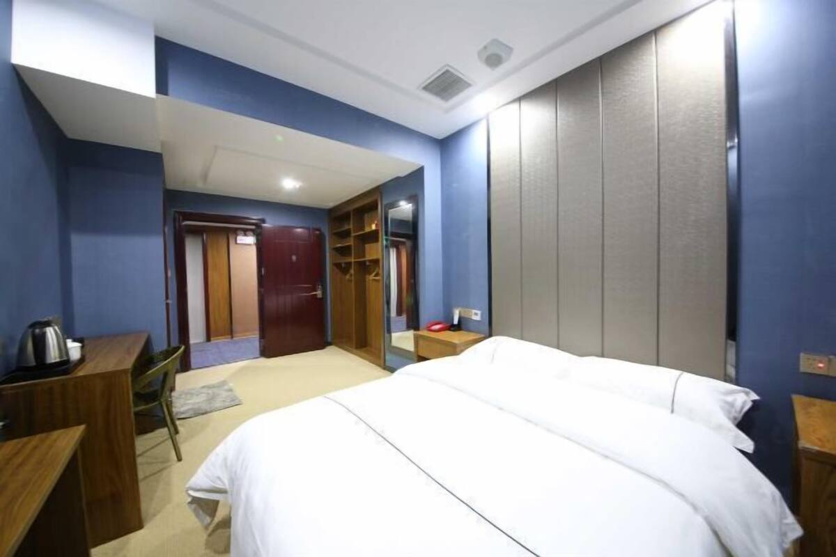 Una habitación de hotel con cama, escritorio, silla, armario y espejo.