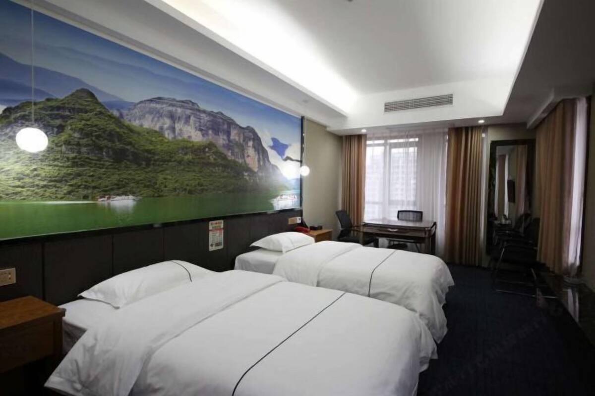 Habitación de hotel con dos camas, un escritorio, una silla, un mural grande en la pared y una ventana con cortinas.