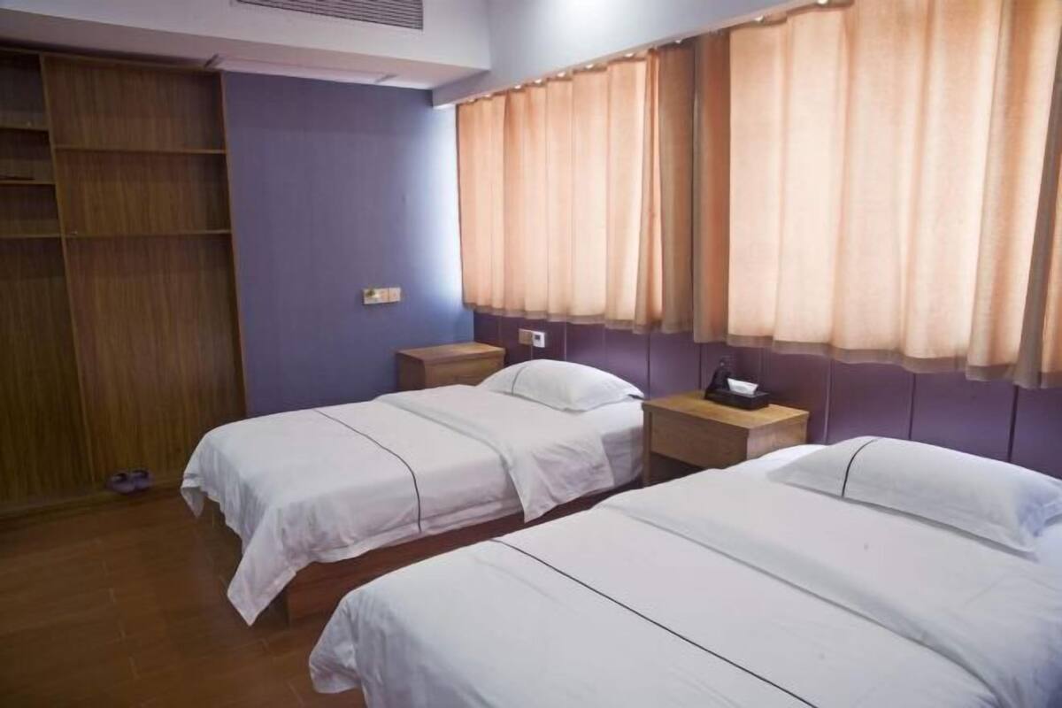 Una habitación con dos camas individuales, un armario de madera y una mesita de noche con lámpara.