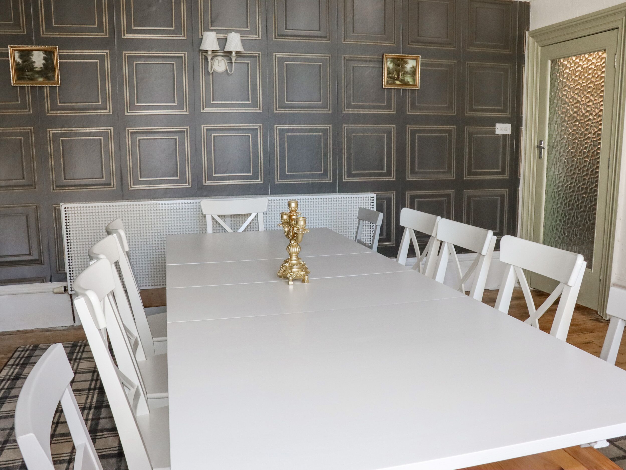 A dining room with a white table and chairs, a decorative candelabra, and a patterned wall with square designs.