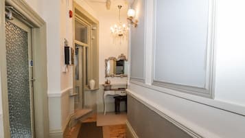 Un couloir doté d’un plancher en bois, d’une porte blanche, d’un miroir et d’un lustre.