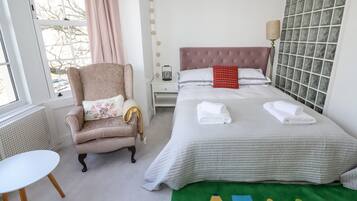 Een keurig opgemaakt slaapkamer met een bed, een stoel, een klein tafeltje en een raam met gordijnen.