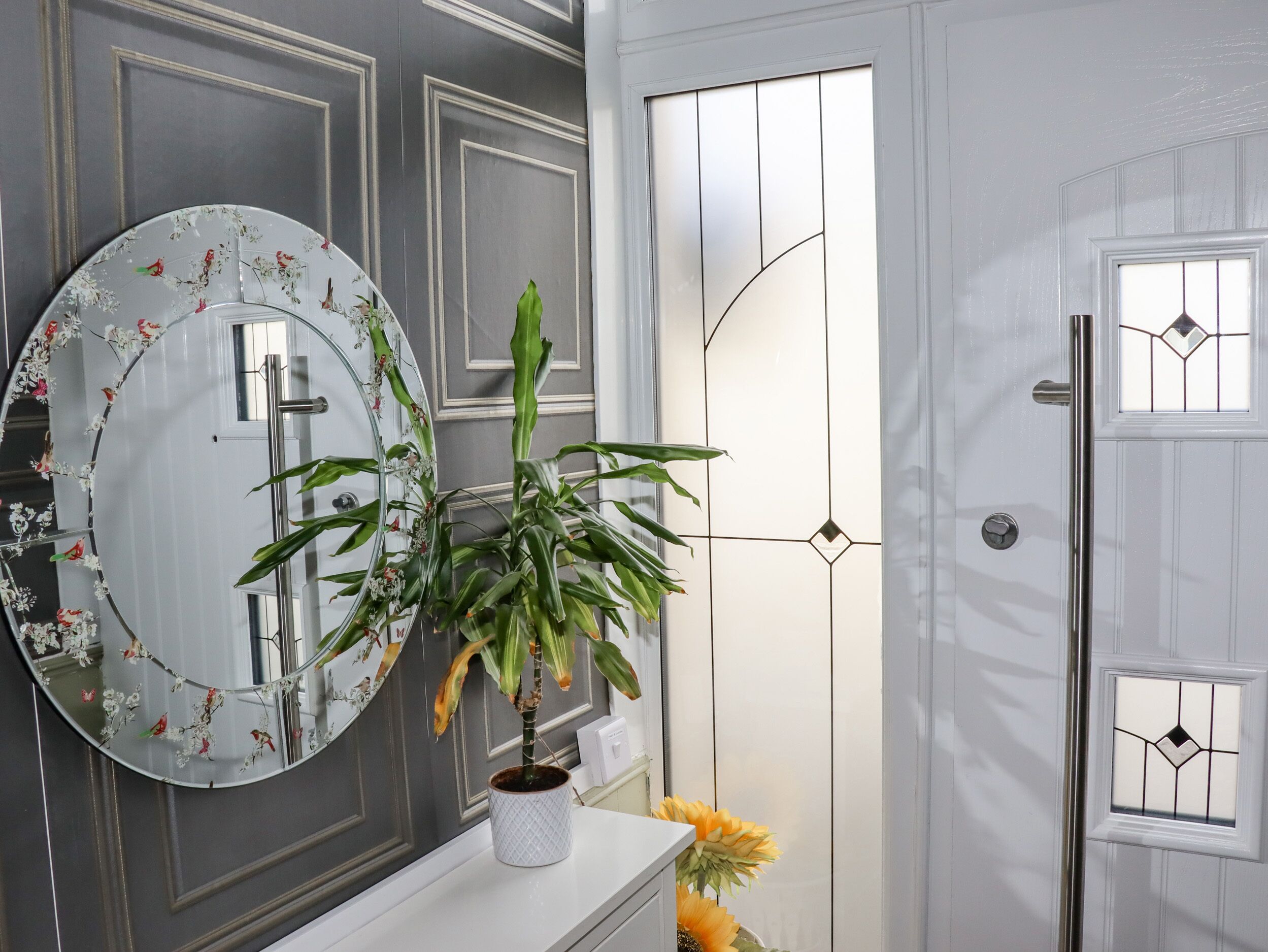 A bathroom with a round mirror, a potted plant, and a door with a geometric glass design.