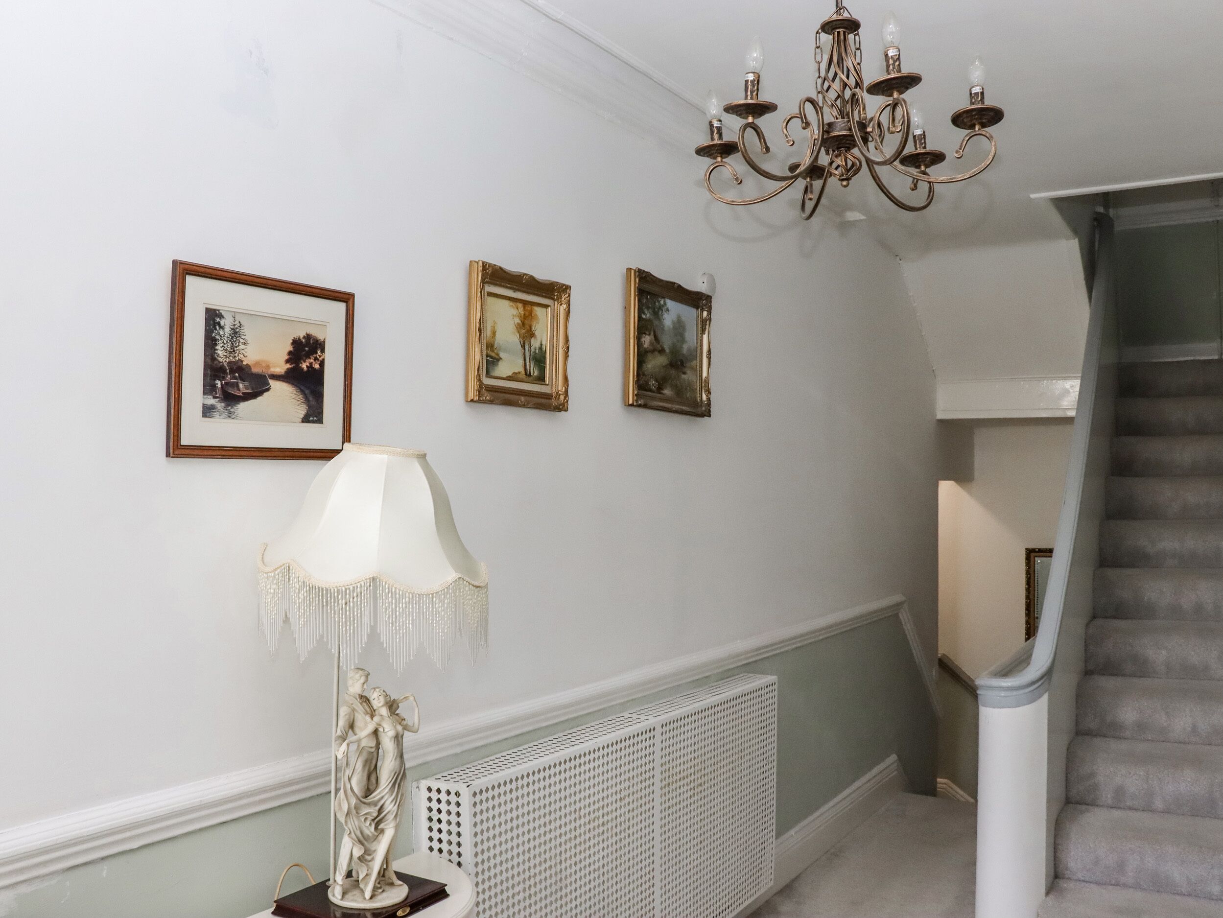 A hallway with a white radiator, a chandelier, and three framed pictures on the wall.