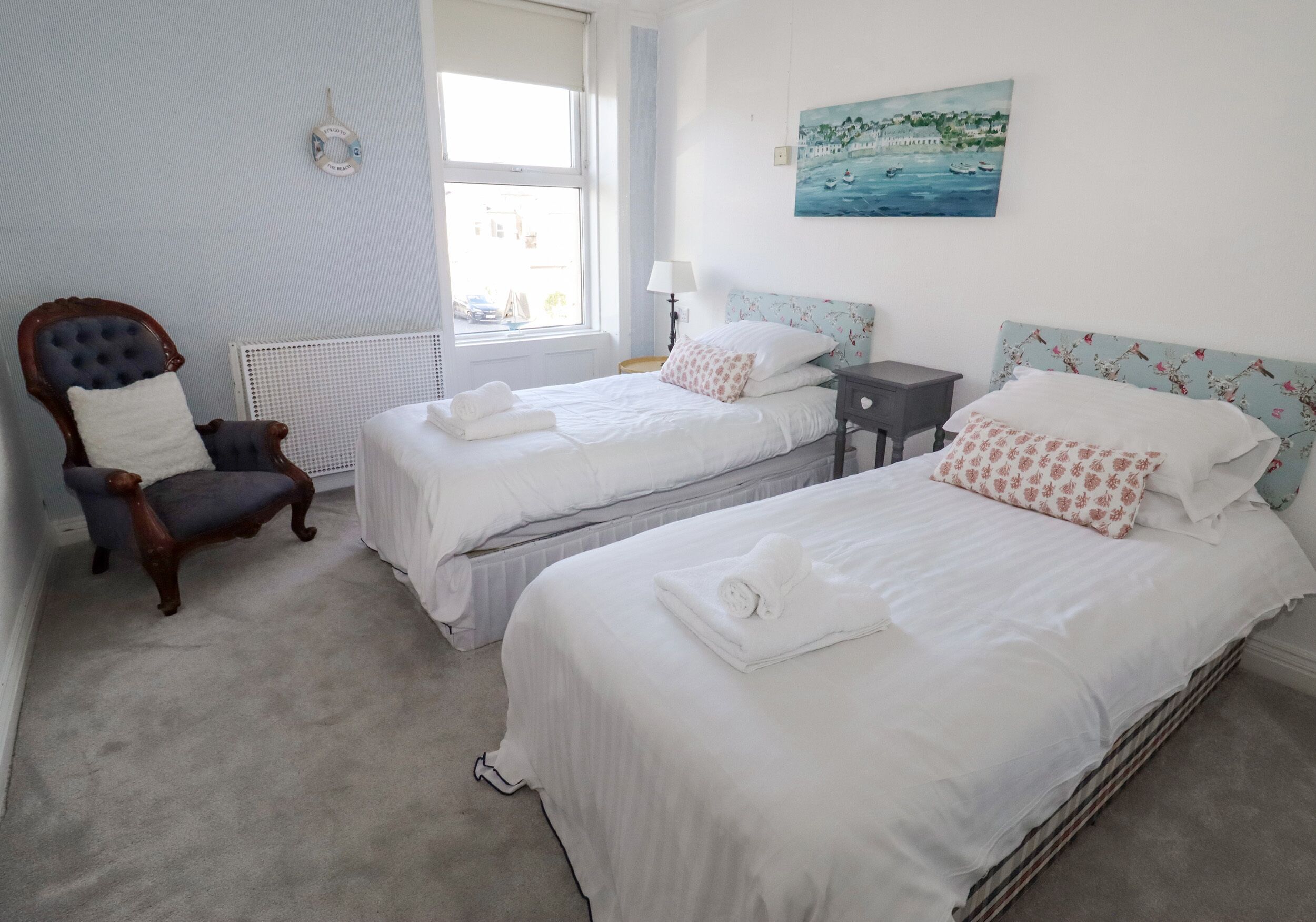 A bedroom with two beds, a chair, a nightstand, and a painting on the wall.