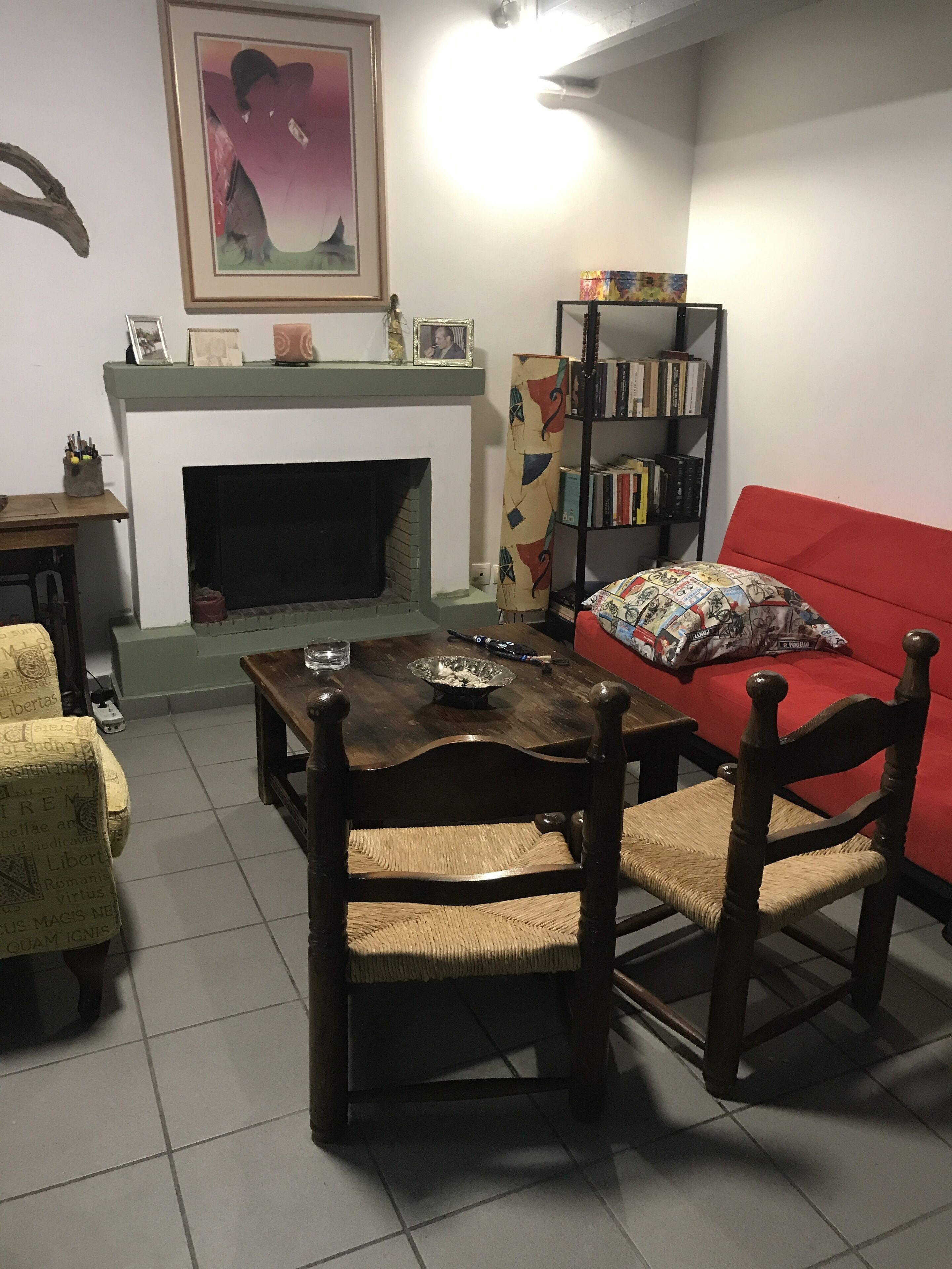 A living room with a fireplace, a red sofa, a wooden dining table with chairs, a bookshelf, and a framed picture on the wall.