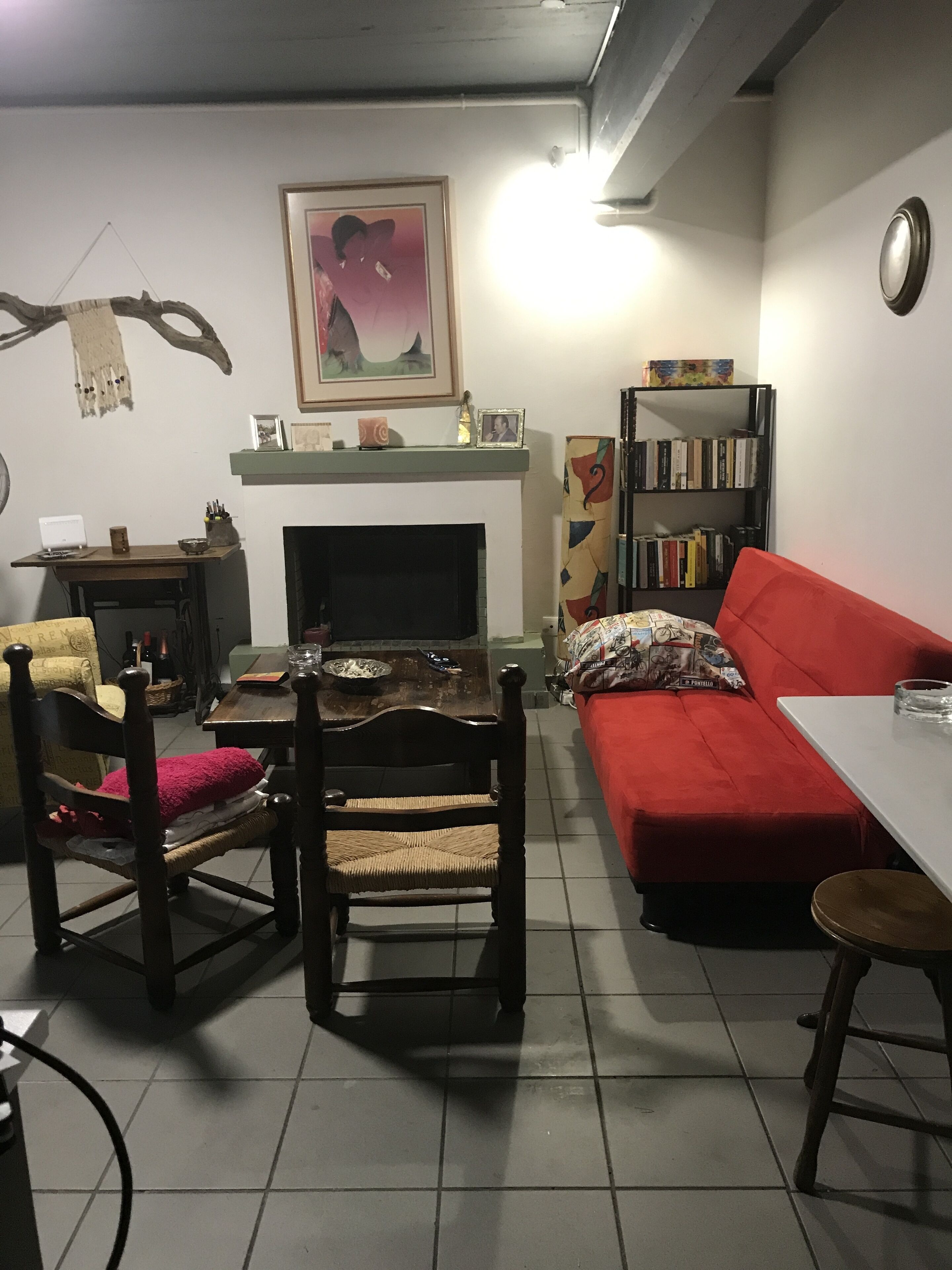 Ein Wohnzimmer mit Kamin, einem roten Sofa, einem Holzstuhl, einem Bücherregal und einem Esstisch.
