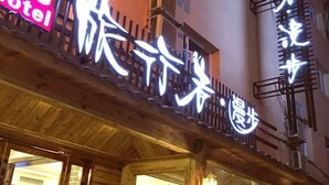 A hotel with a wooden facade and illuminated signage in a foreign language. - Lvxingzhe Manbu Theme Hotel (Zhangjiajie)