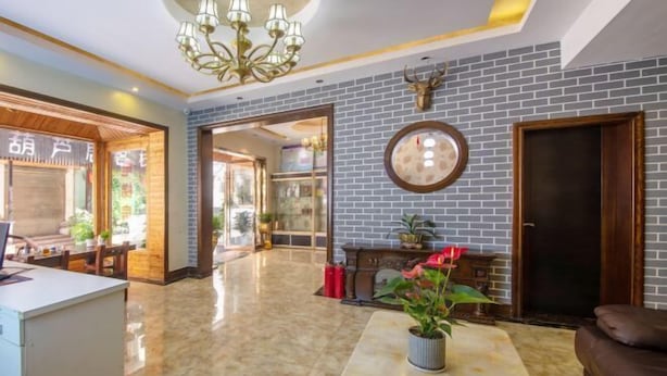 A lobby with a marble floor, a reception desk, a chandelier, a brick wall with a mounted deer head, and a potted plant. - Lvxingzhe Manbu Theme Hotel (Zhangjiajie)