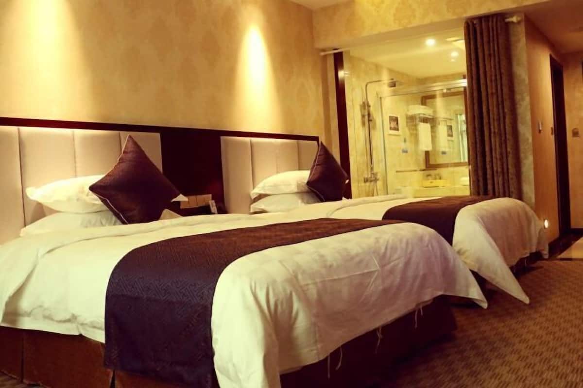 A hotel room with two beds, a large mirror, and a bathroom visible through an open door.