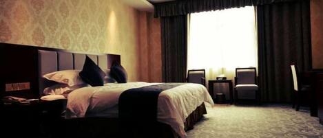 Ein Hotelzimmer mit einem großen Bett, einem Nachttisch, einem Schreibtisch, einem Stuhl und einem Vorhangfenster.