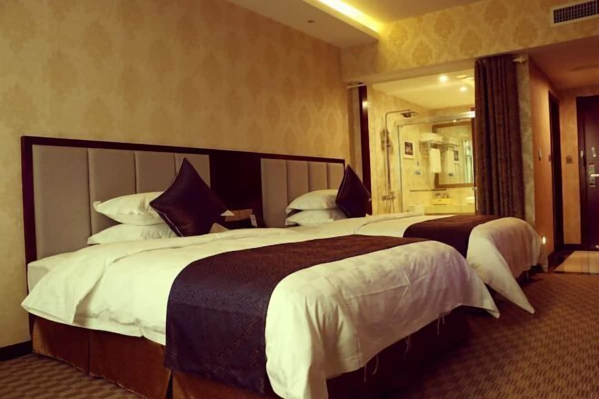 A hotel room with two beds, a large mirror, and a bathroom visible through an open door.