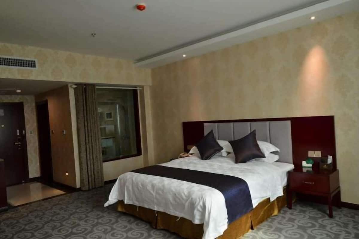 A hotel room with a large bed, a nightstand, a mirror, and a door leading to a bathroom.