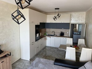 Una cocina moderna con armarios blancos, una encimera negra y una zona de comedor con sillas blancas.