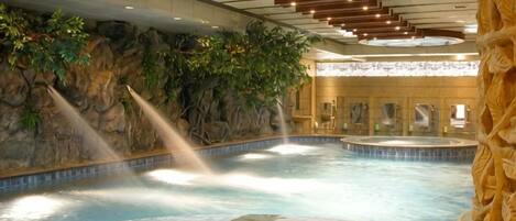 A hot spring area with multiple pools, a rock wall with greenery, and a large column.