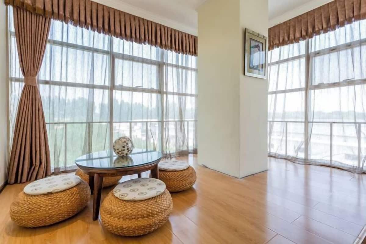 A room with large windows, a glass table, and four woven ottomans with cushions.
