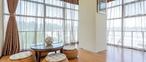 A room with large windows, a glass table, and four woven ottomans with cushions.
