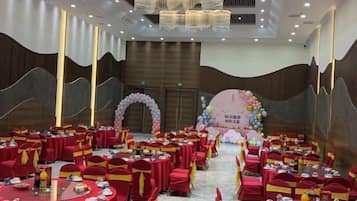Un salón de banquetes con mesas redondas, sillas rojas y un escenario con un fondo floral.