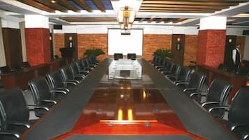 Una sala conferenze con un lungo tavolo, sedie, un podio e uno schermo in prima fila.