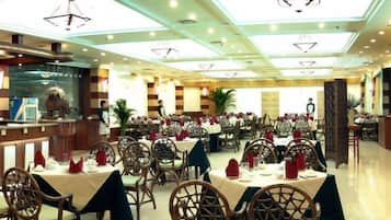 Un restaurante con mesas y sillas redondas, una zona de bar e iluminación empotrada en el techo.