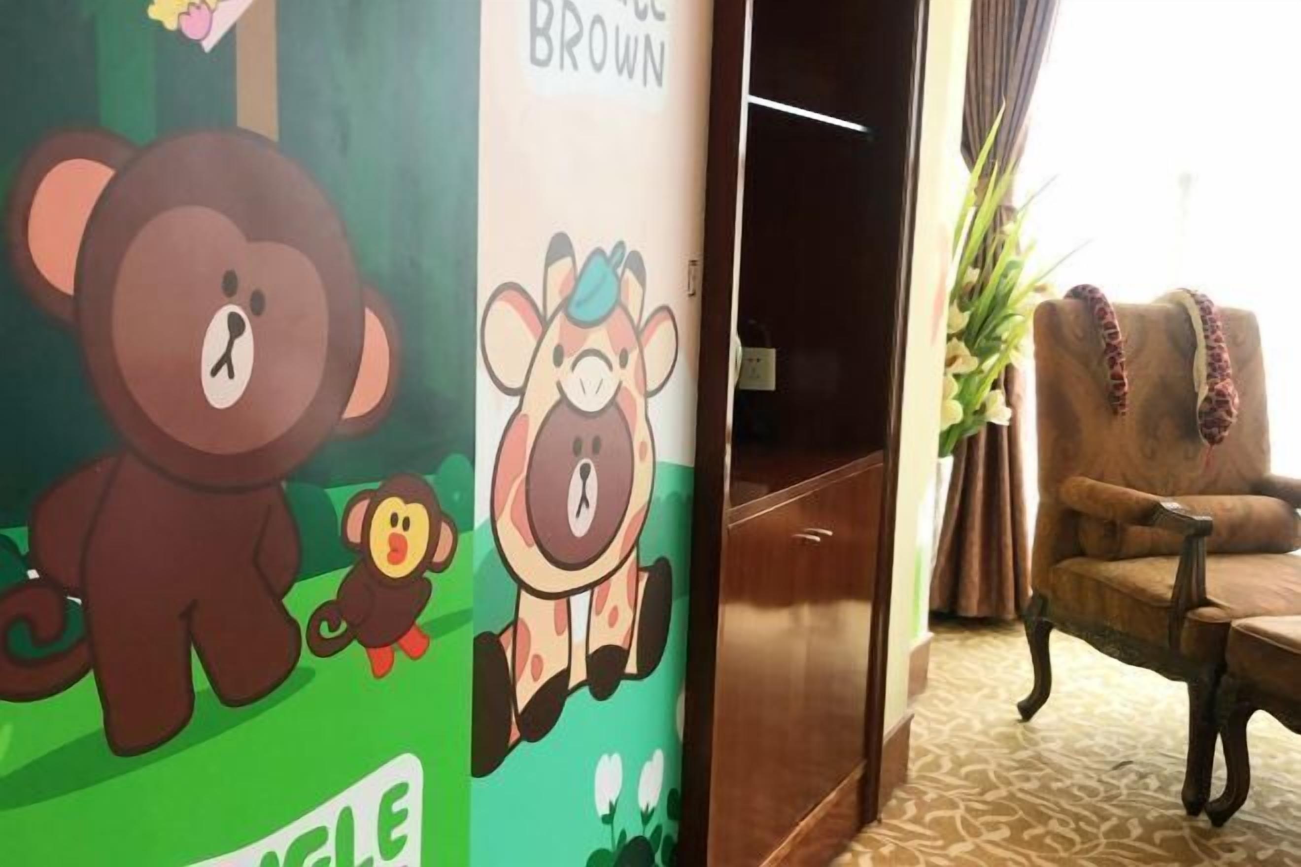Un vestíbulo de hotel con una pared verde decorada con ilustraciones de animales animados, una silla de madera y una alfombra estampada.