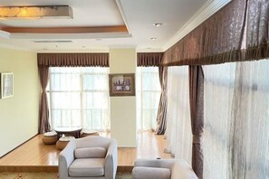 A spacious living room with a sofa, ottoman, and a small table, large windows with curtains, and a ceiling light fixture. - Tianhaoyuan Country Club (Beijing)