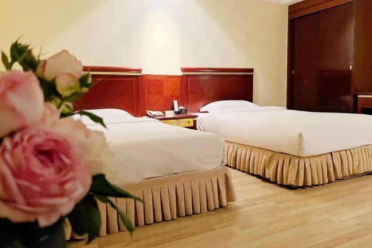 A hotel room with two beds, wooden headboards, a bedside table with a phone, and a wooden floor.