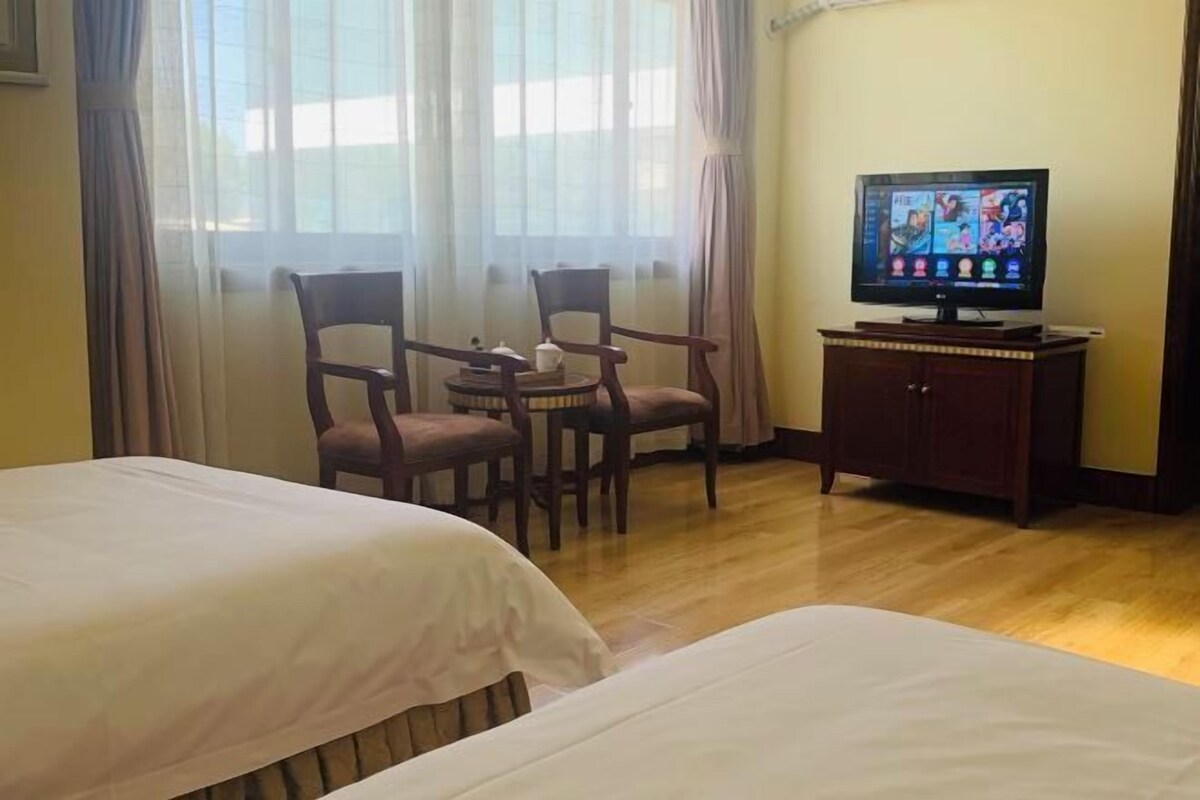 A hotel room with two beds, a television on a cabinet, and a table with chairs.
