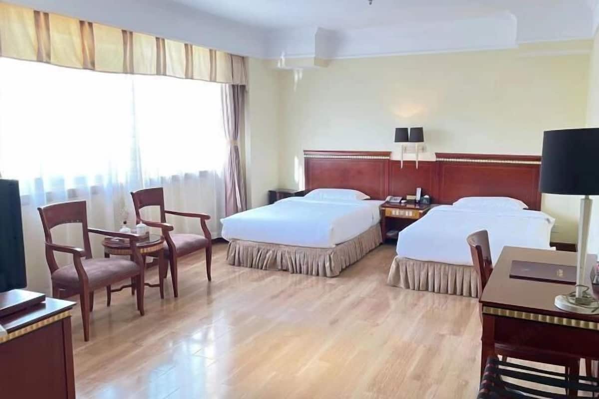 A hotel room with two beds, a desk, a chair, and a small table.