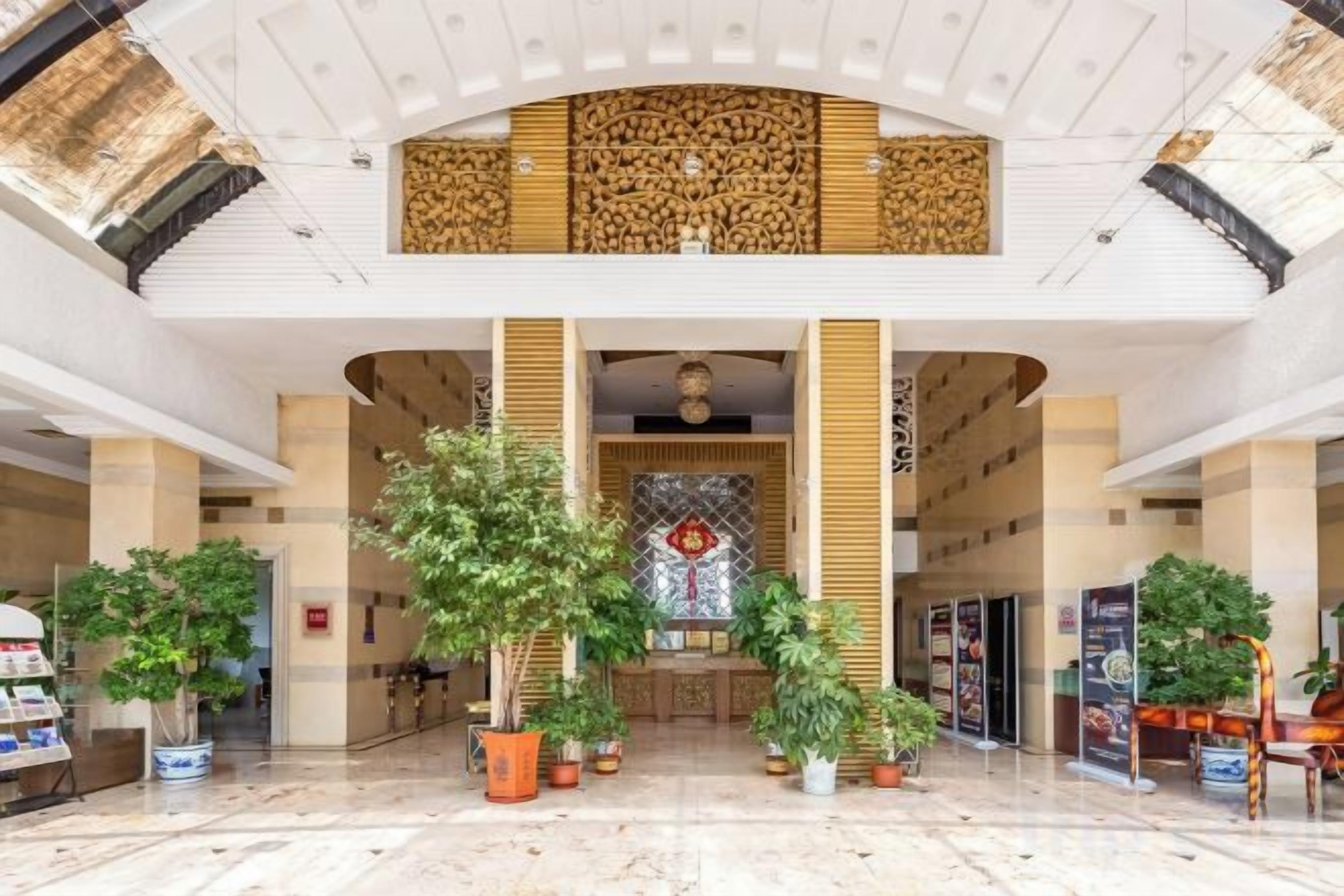 Un hall d’entrée spacieux, doté d’un haut plafond, de grandes colonnes et de plantes en pot.