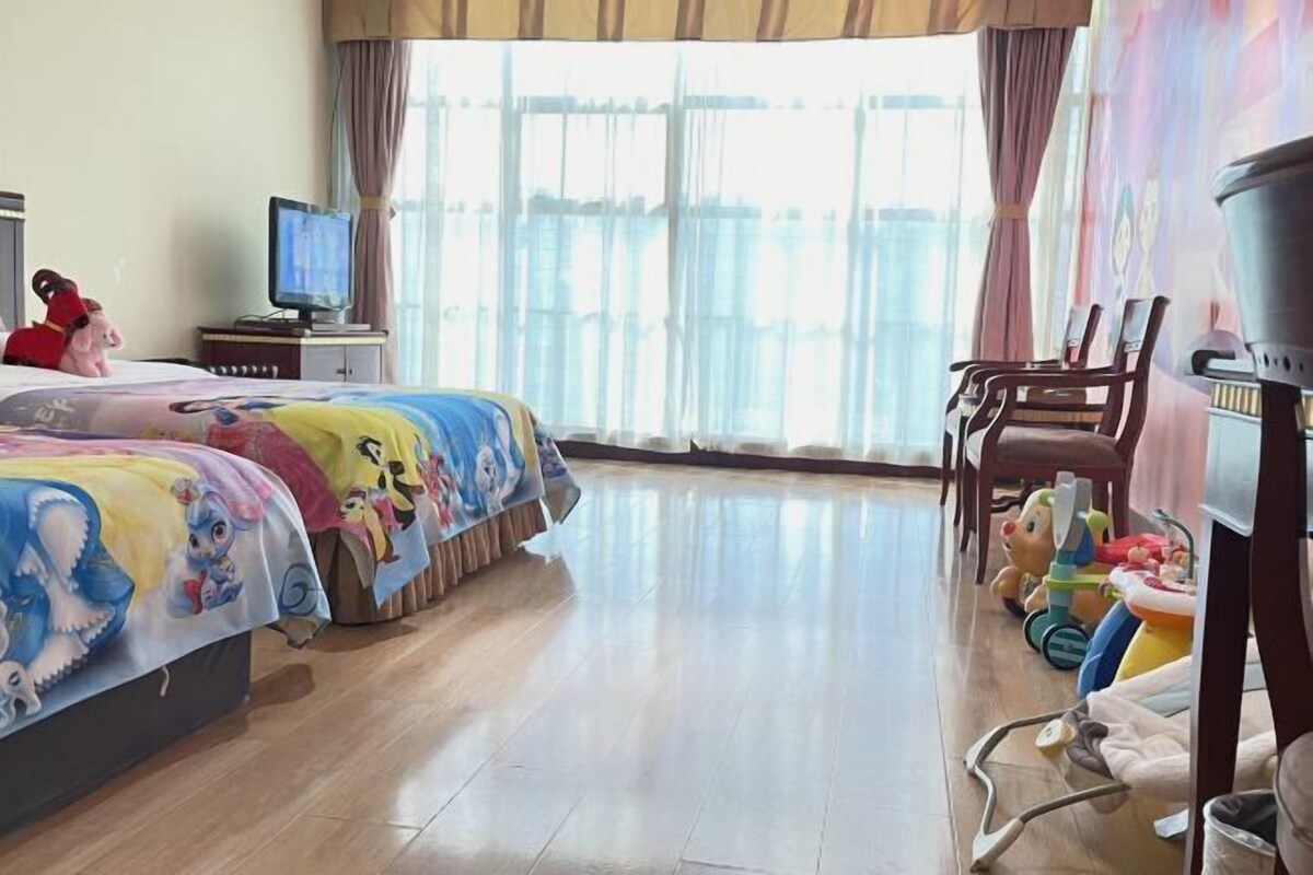 A hotel room with two beds, a television, a window with curtains, and a view of the outside.