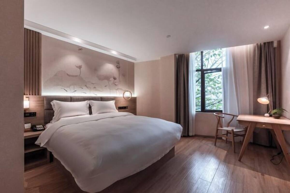 Une chambre moderne avec un grand lit, une table de chevet, un bureau, une chaise et une œuvre d’art accrochée au mur.