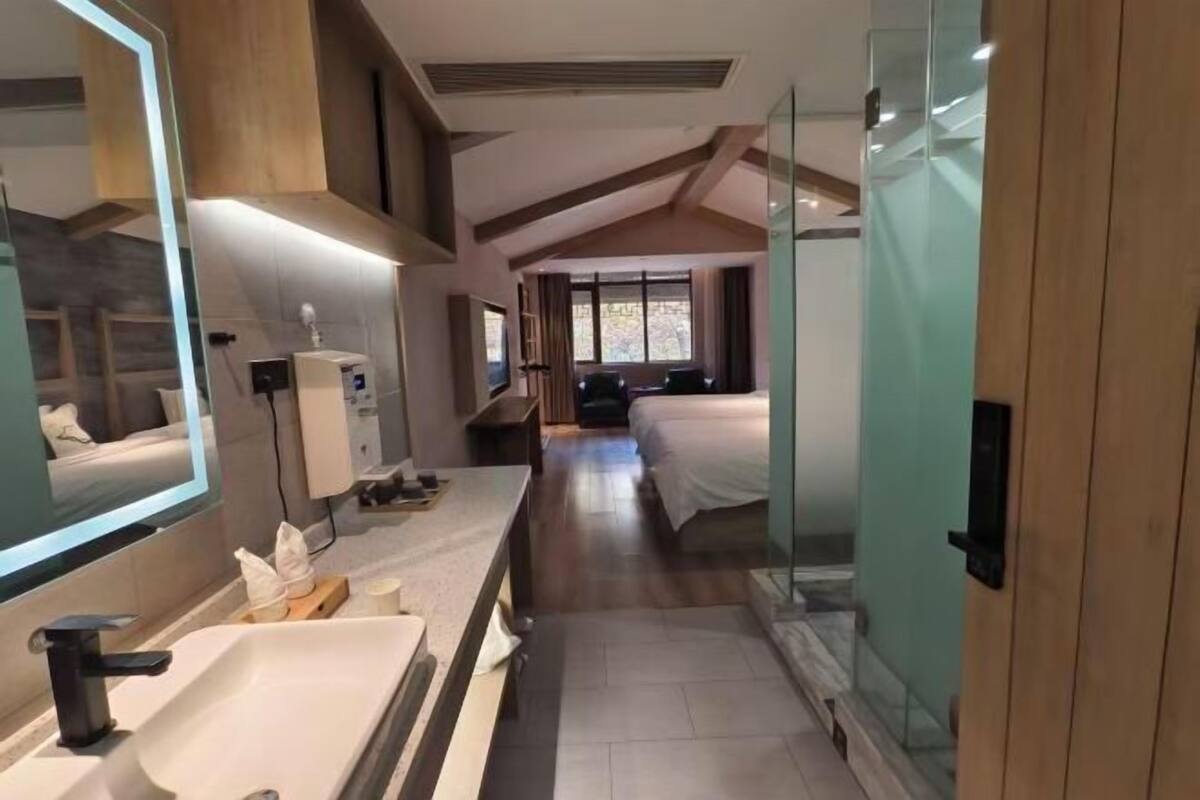 Une chambre d’hôtel moderne avec un grand miroir, un lavabo, une table de chevet, un lit et une fenêtre.