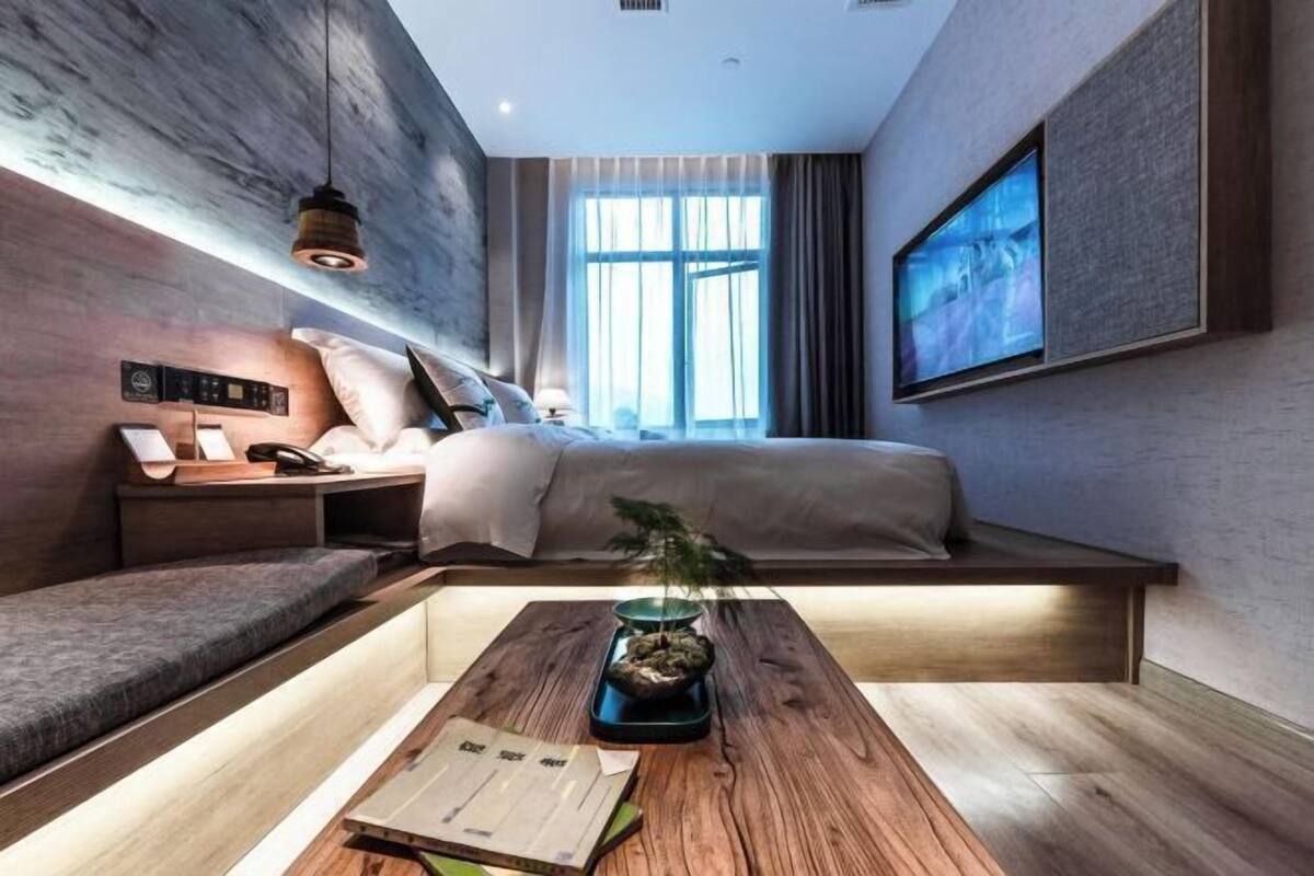 Une chambre d’hôtel moderne équipée d’un lit, d’une table de chevet, d’une lampe et d’un grand téléviseur fixé au mur.