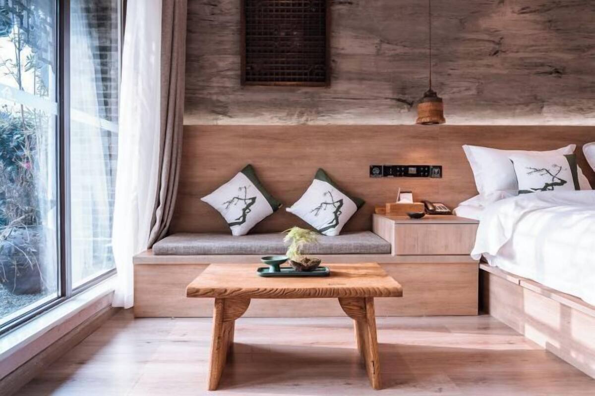 Une chambre moderne avec une tête de lit en bois, une table de chevet, une commode et une fenêtre donnant sur un paysage verdoyant.