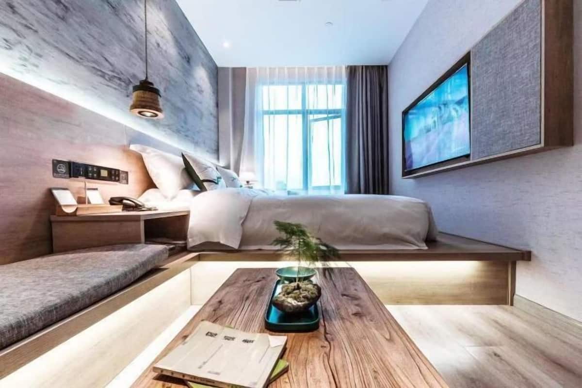 Une chambre d’hôtel moderne équipée d’un lit, d’une table de chevet, d’une lampe et d’un grand téléviseur fixé au mur.