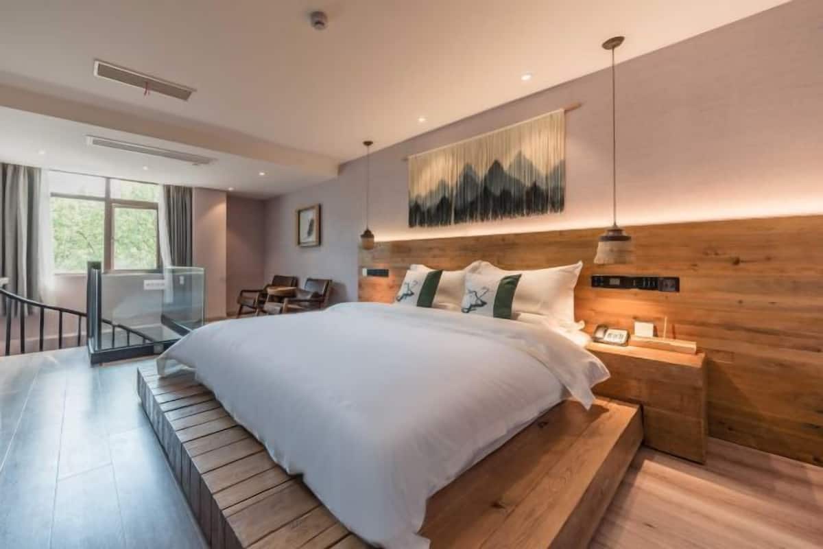 A modern bedroom with a large bed, wooden headboard, bedside tables, and a view of the outdoors.