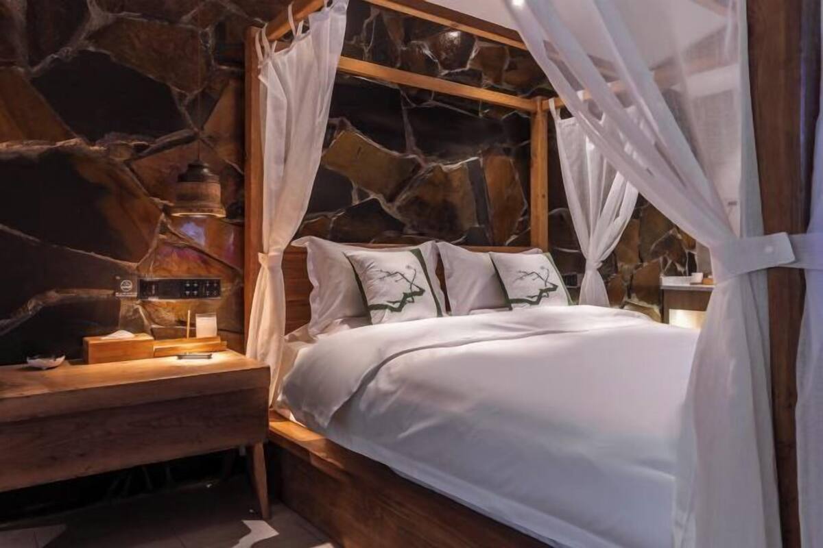 Un lit à baldaquin avec une literie blanche et des coussins décoratifs, placé devant un mur en pierre.