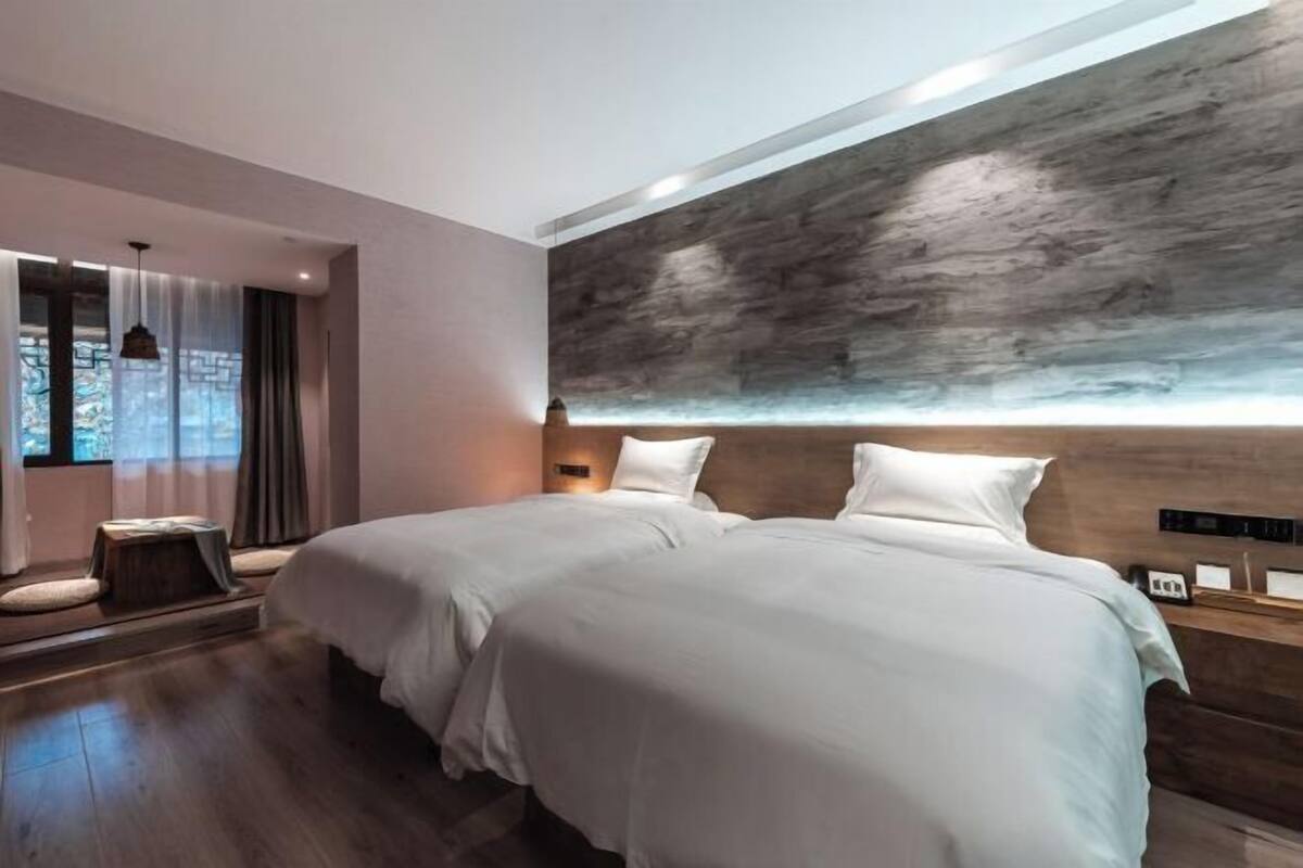 Une chambre d’hôtel moderne avec deux lits, un mur décoratif en bois et une petite table de chevet avec une lampe.