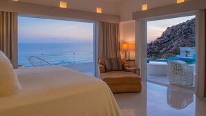 Habitación de hotel con una cama grande, una silla, una lámpara y vistas al océano y a una piscina.