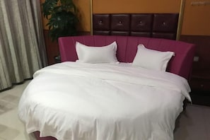 Un lit bien fait, avec une literie blanche et une tête de lit violette, dans une chambre d'hôtel.