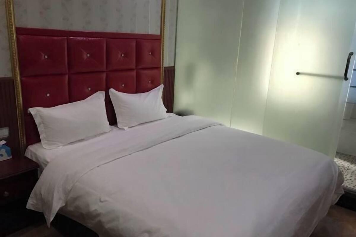 A bed with a red headboard, a white bedspread, and a nightstand with a tissue box.