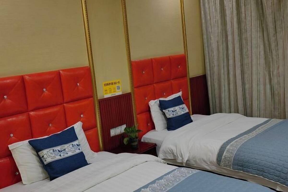 A hotel room with two beds, red headboards, and a curtain on the window.
