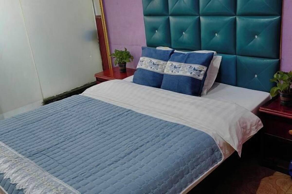 A bed with a blue quilt, a teal headboard, and two bedside tables with potted plants.