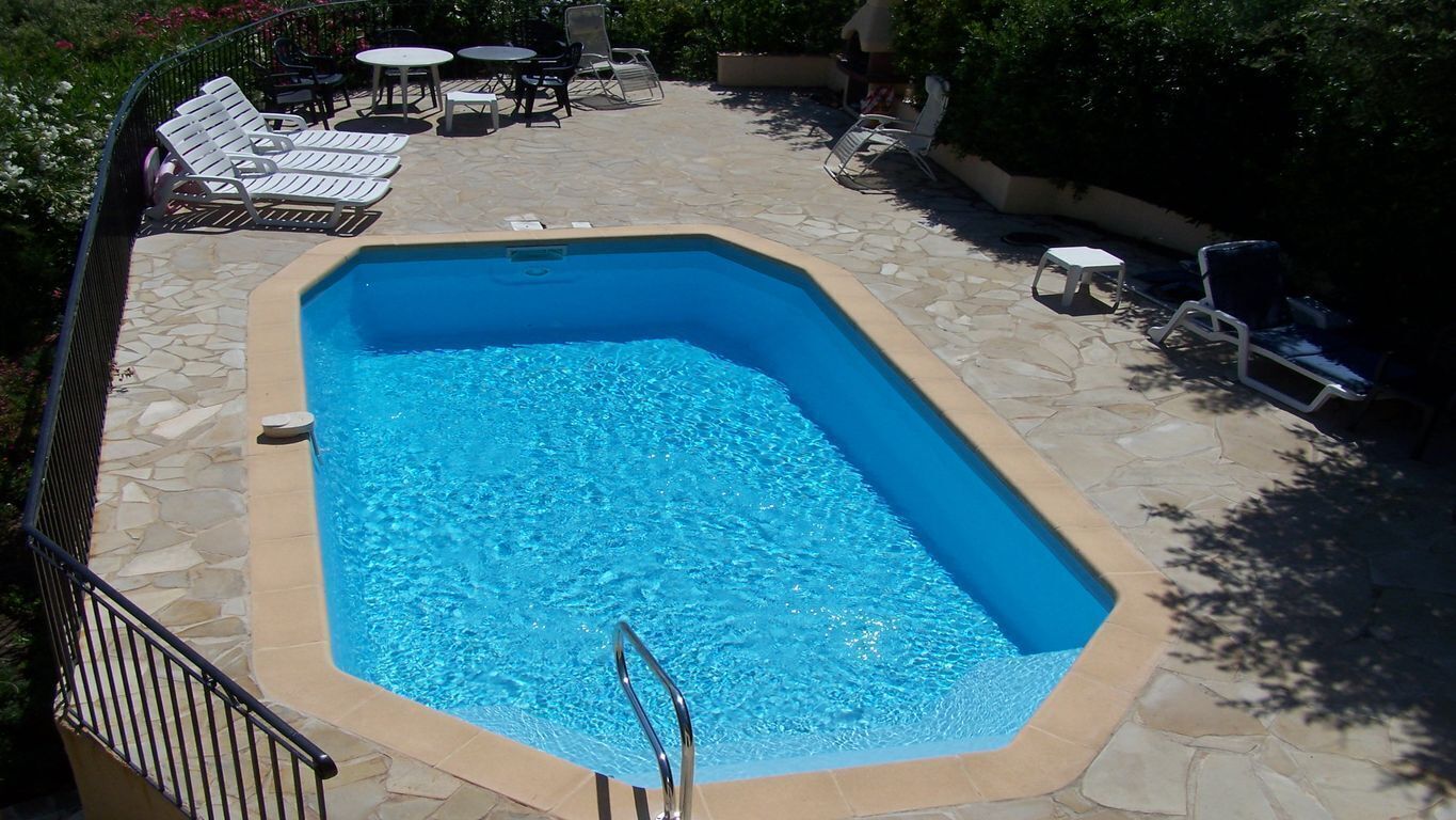 Una piscina con borde de piedra, rodeada de sillas y mesas de descanso.