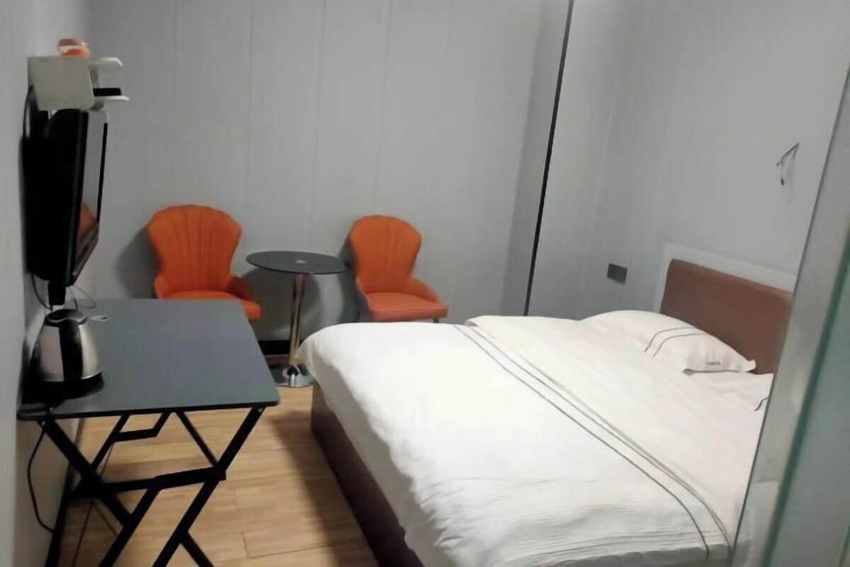 Une petite chambre d’hôtel avec un lit, deux fauteuils orange, une petite table et un téléviseur.