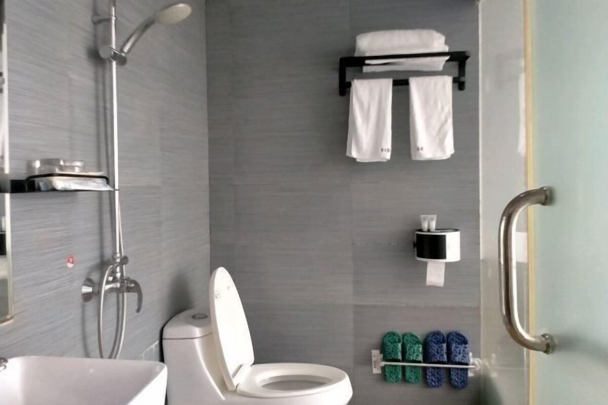 Une salle de bain moderne équipée d’une douche, de toilettes et d’un lavabo. Des serviettes et des chaussons sont accrochés au mur.