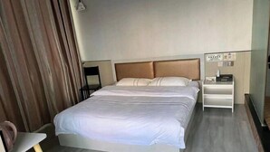 Une chambre d’hôtel avec un lit, une table de chevet, une chaise et un rideau.